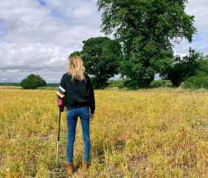 Back of woman with walking stick facing a yellow field