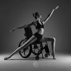 Hannah Todd Photography Kate dancing from her wheelchair with right leg full extended on the ground behind her and left arm extended above her head.