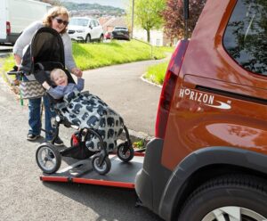 Victoria Machin Horizon Mother wheeling her son's wheelchair up the ramp of their wheelchair accessible vehicle (WAV). Mother and son are smiling.