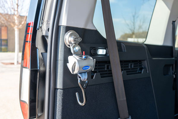 A close-up of a car's interior shows a seat belt and a mounted mobility aid device with a hook, designed to assist with lifting or securing objects in the vehicle.