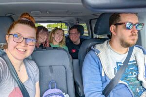 Jenni and her partner sit in the front seats with Imali, her partner and carer in the back. They all smile at the camera.