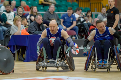 wheelchair rugby player on the court rolling at speed with rugby ball on lap