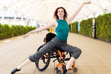 Dancer, Kate Stanforth, poses on her chair with toes pointed to the left and arms raised