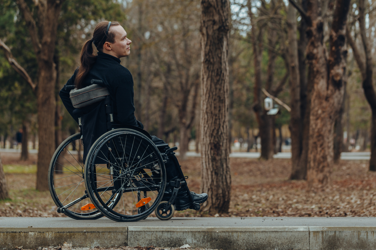 Young disabled man in wheelchair walking park