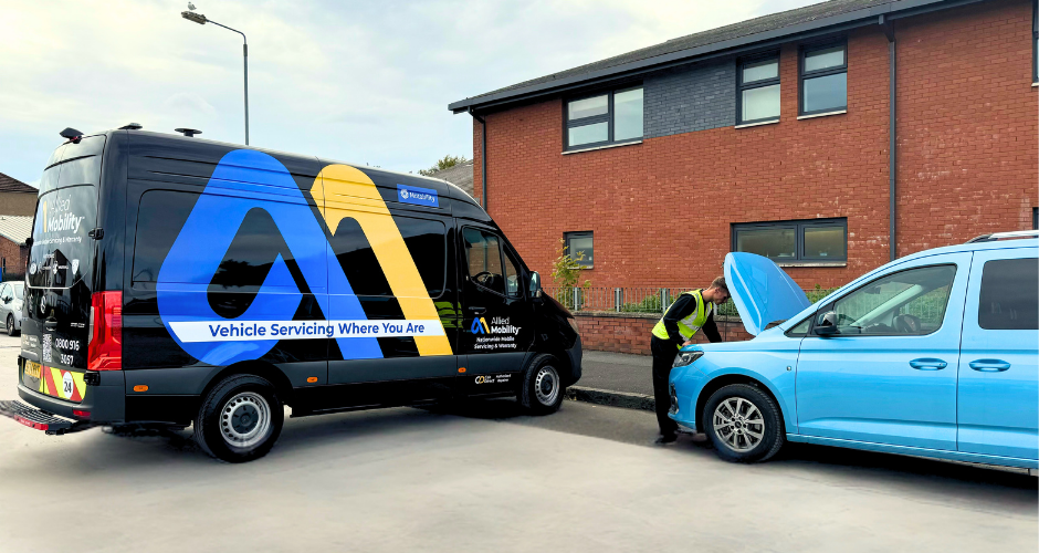 Automotive mechanic under the bonnet of a WAV with a mobile servicing van behind him.