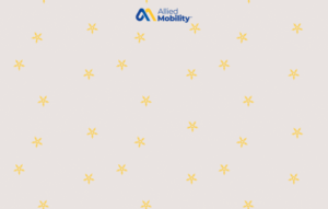 Cars with headlights on drive through heavy snow on a winter road at dusk. Text reads: Tips & Tricks for Driving Your WAV in the Winter. Allied Mobility logo in blue and yellow in corner.