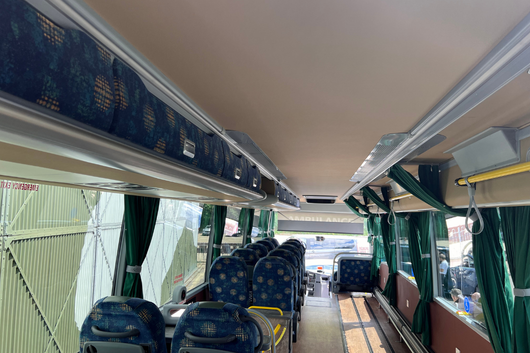 Interior view of a Jumbulance coach, showing rows of seats, overhead storage, green curtains and a wide central aisle designed for wheelchair access.