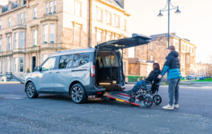 wheelchair accessible vehicle with a rear ramp lowered on a city street, allowing a wheelchair user to enter.