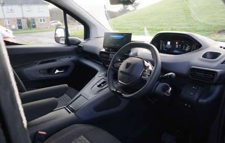 Driver’s view of a modern vehicle interior showing the steering wheel, dashboard, digital displays and front passenger seating.