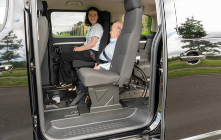 Interior of a wheelchair accessible vehicle showing the wheelchair user positioned next to a row two seated passenger.