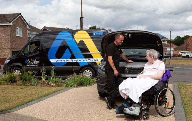 Allied Mobility service van parked on a residential street while a technician assists a wheelchair user beside an open vehicle bonnet.