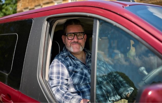 Nick Wilson behind the wheel of his red wheelchair accessible vehicle (WAV), Ford Dream.