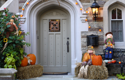 Front entrance decorated for autumn with scarecrows, pumpkins, straw bales, orange fairy lights, and a wheelchair accessible vehicle parked nearby.
