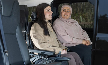 Two women sitting inside a WAV, with one person seated in an electric wheelchair.